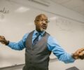 Well dressed ablack instructor in front of white board teaching